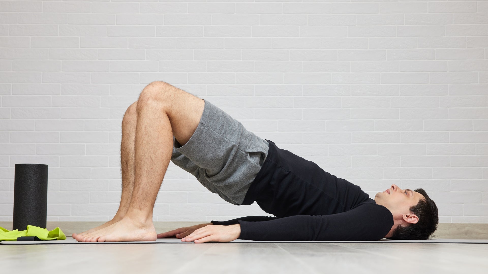 Person lying on a yoga mat performing a leg lift exercise against a light gray wall.