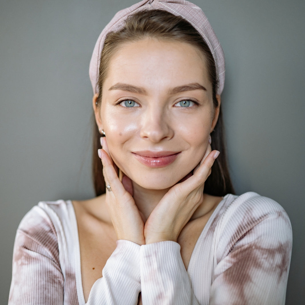 Woman with a pink headband and white top against a gray background