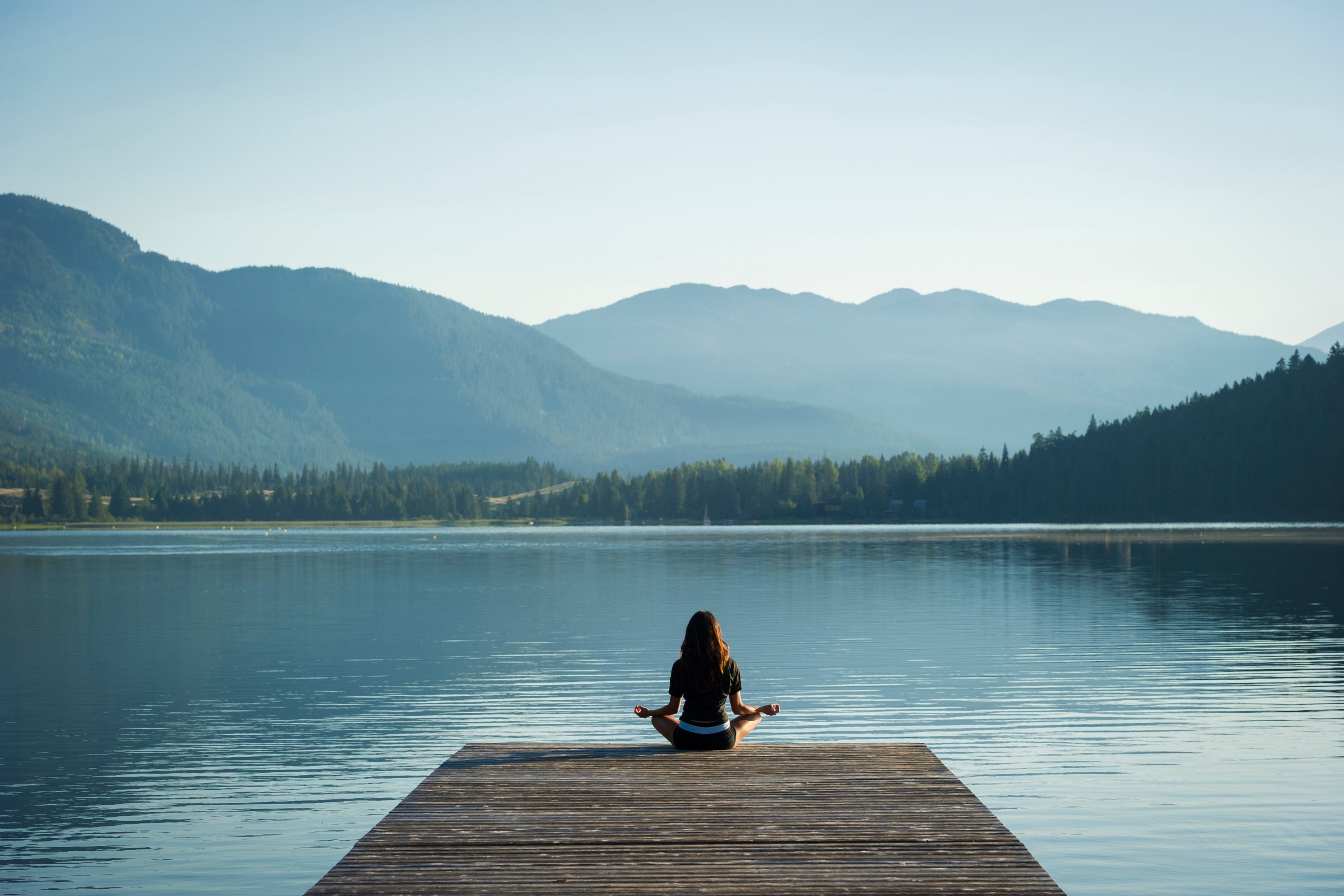 Person meditating on a dock by a lake with mountains in the background