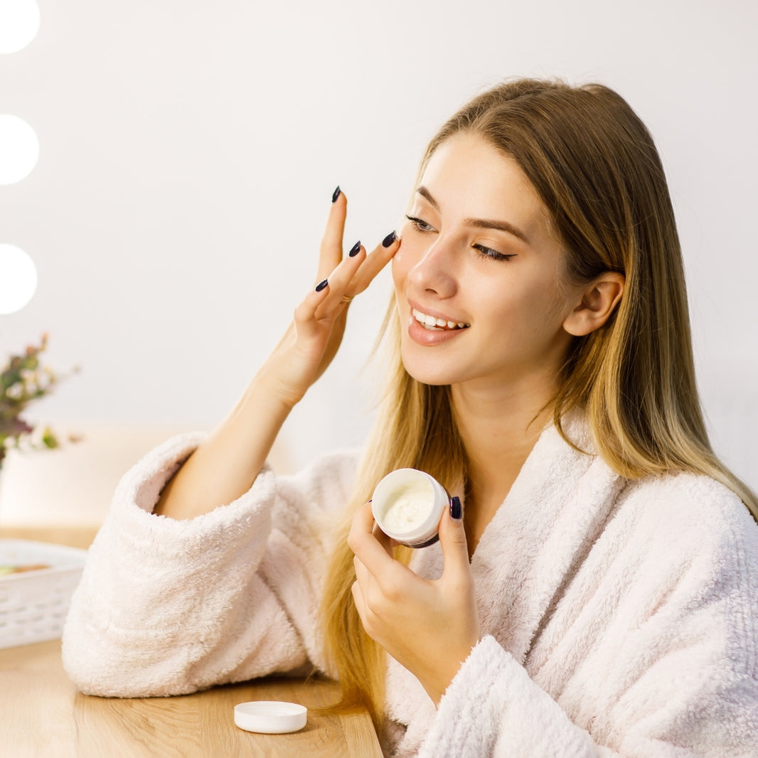 Woman applying cream to her face in a cozy room.